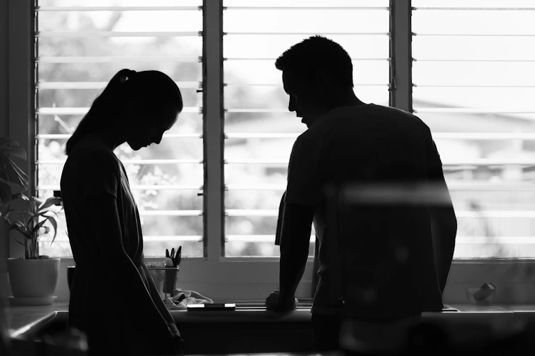 A woman with her head down faces a man who looks angry.