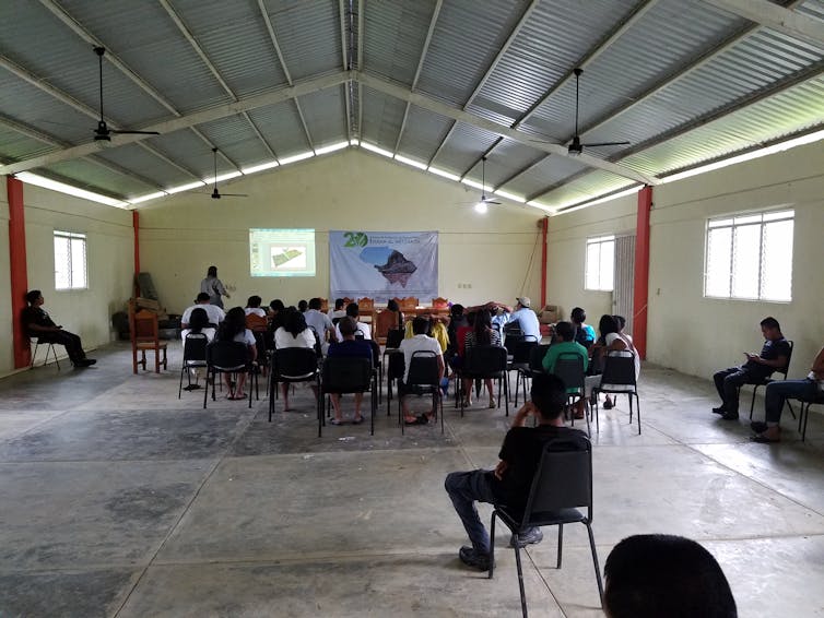 El mapeo aéreo lidar puede revelar sitios arqueológicos mientras se observa a los pueblos indígenas y sus conocimientos. 4 Vista interior de varias decenas de personas sentadas en sillas mirando al presentador.