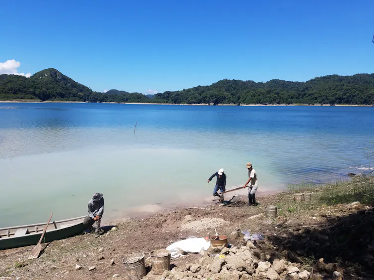people along the shoreline of a body of water lifting a stone object