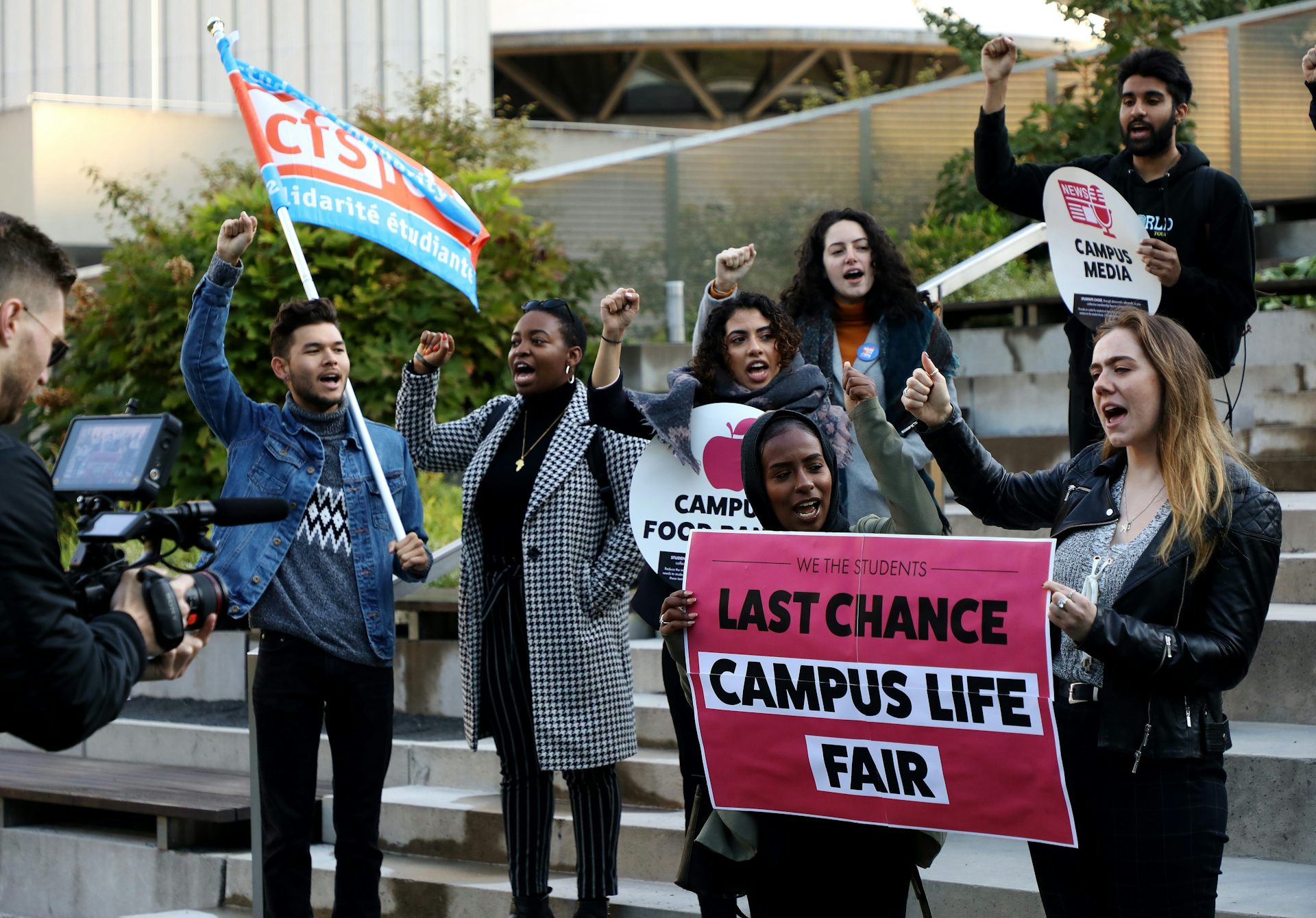 People protest on steps with a sign that says last chance campus life fair.