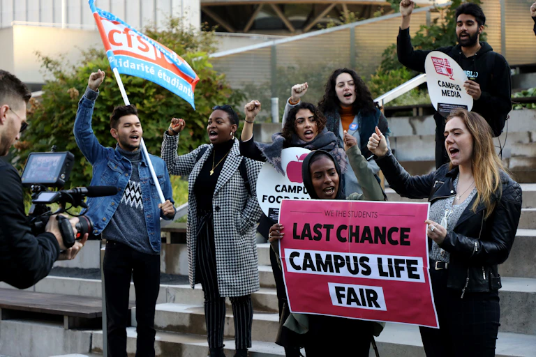 People protest on steps with a sign that says last chance campus life fair.
