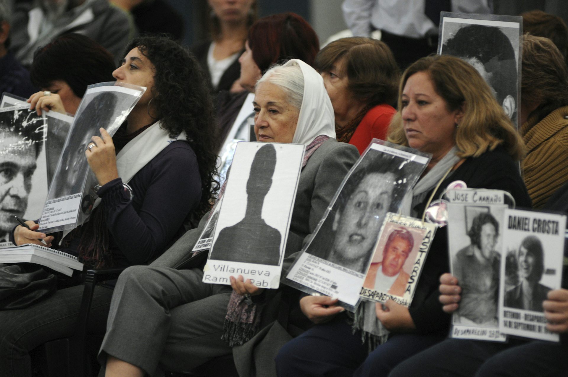 Seated women, some wearing the white banadana, hold black and white photos of missing loved ones.