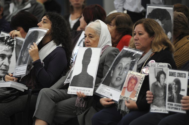 Seated women, some wearing the white banadana, hold black and white photos of missing loved ones.