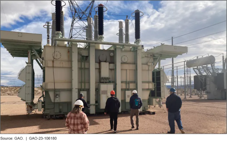 people wearing hardhats in front of electrical equipment the size of a small house