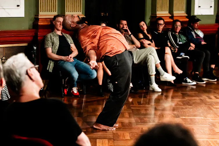 A man bends over backwards in front of an audience.