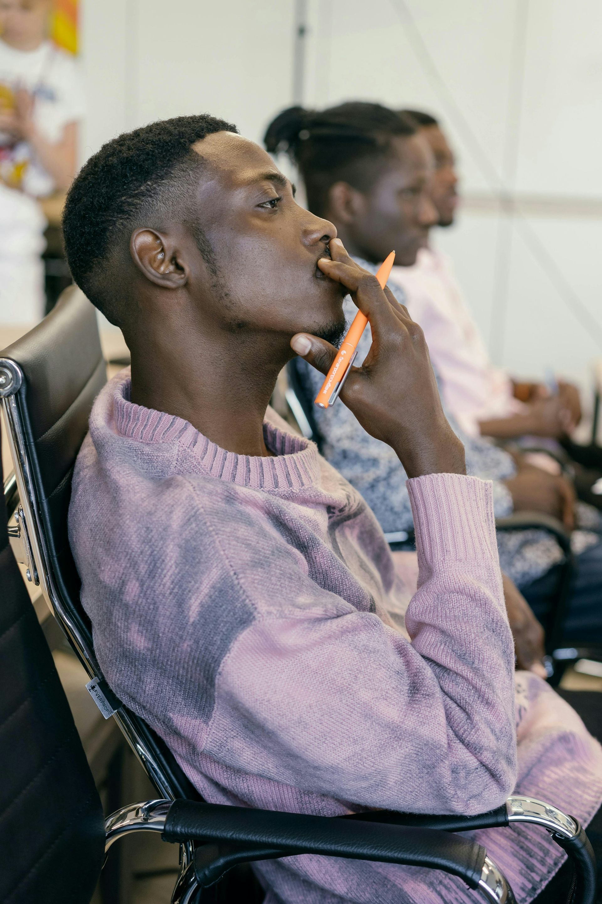 Man sits in chair in a lecture with a pencil to his lip, deep in thought.