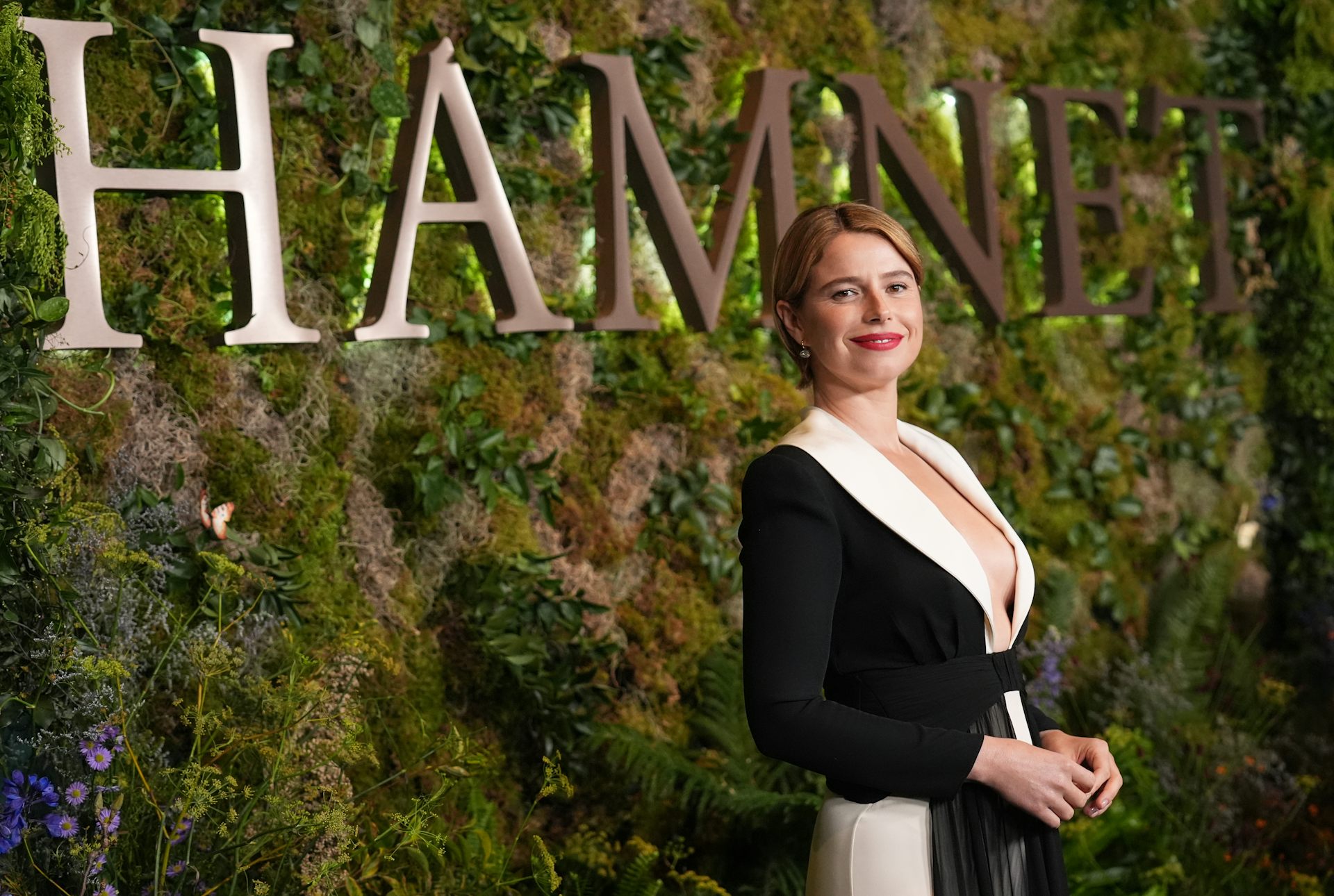 A woman in fancy v-neck dress in front of a mossy green backdrop.