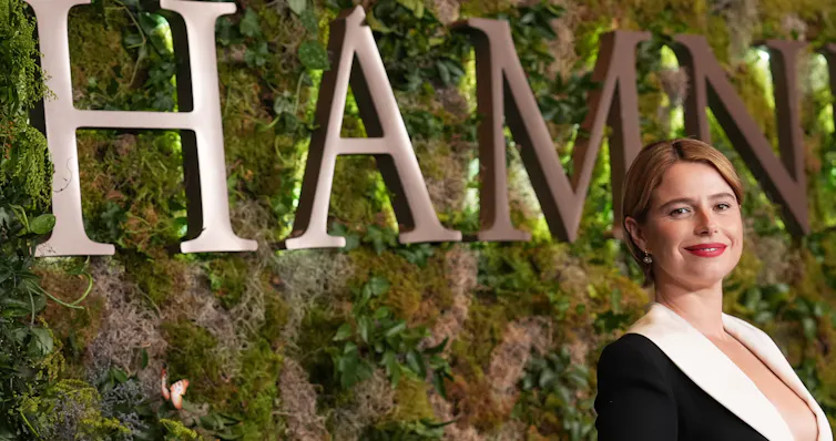 A woman in fancy v-neck dress in front of a mossy green backdrop.