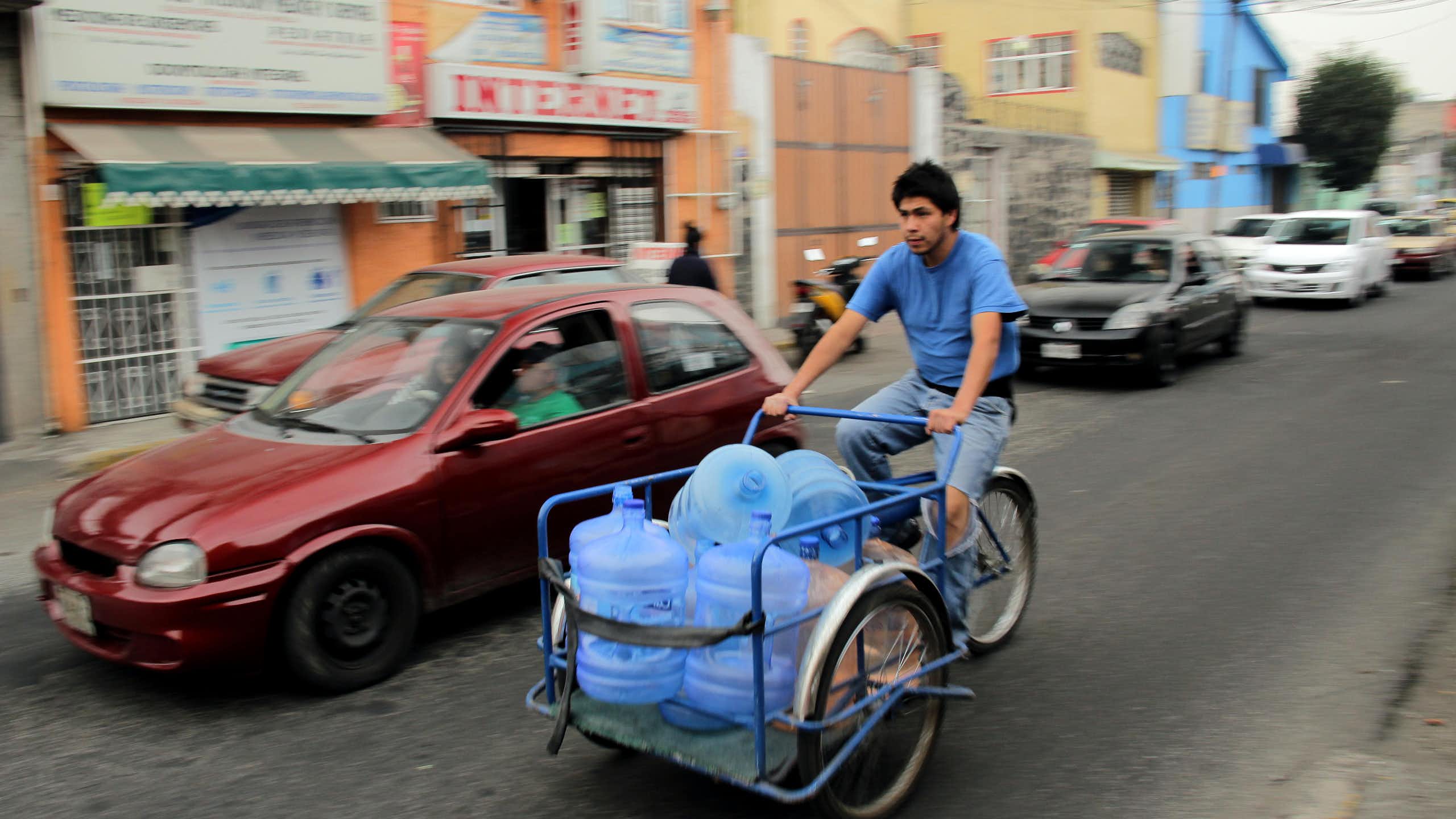A man on a bicycle carrying water bottles.