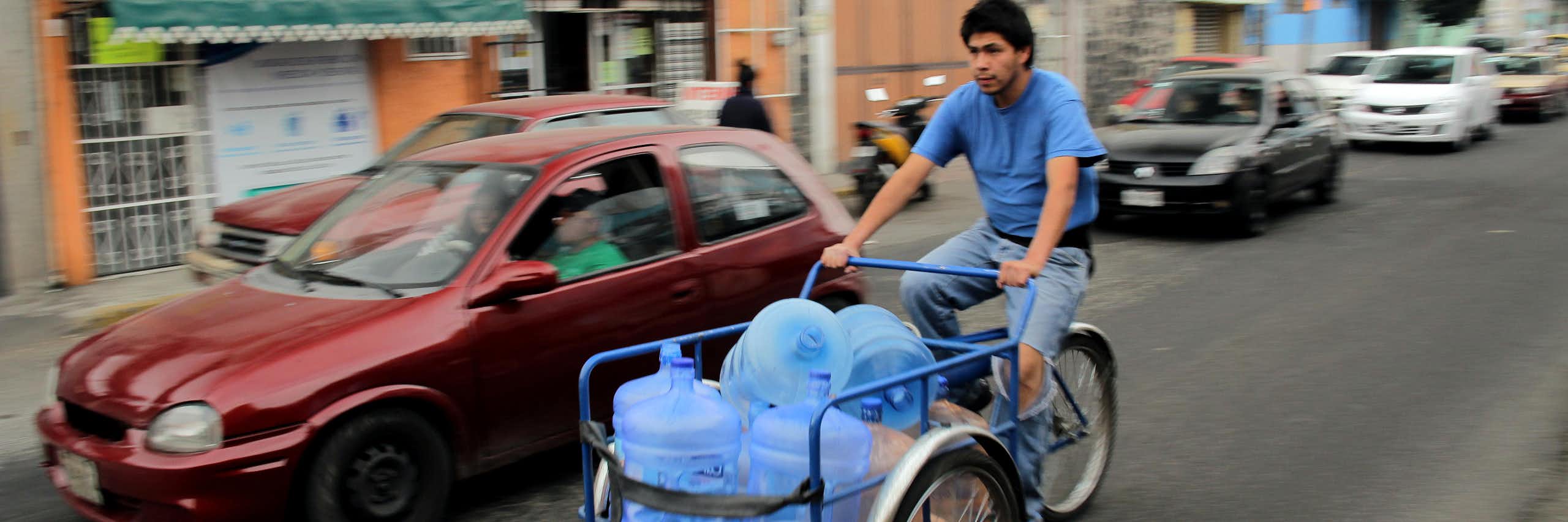 A man on a bicycle carrying water bottles.