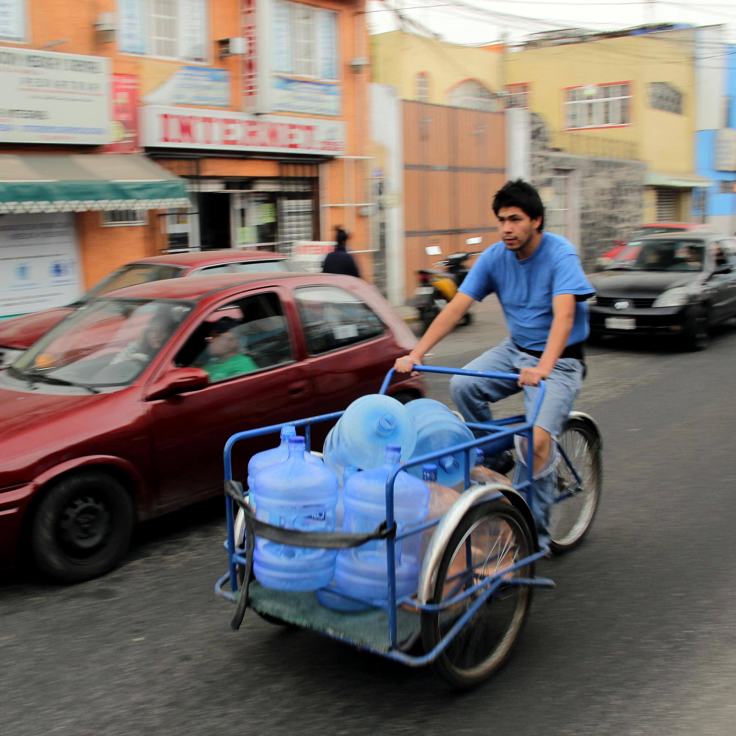 A man on a bicycle carrying water bottles.