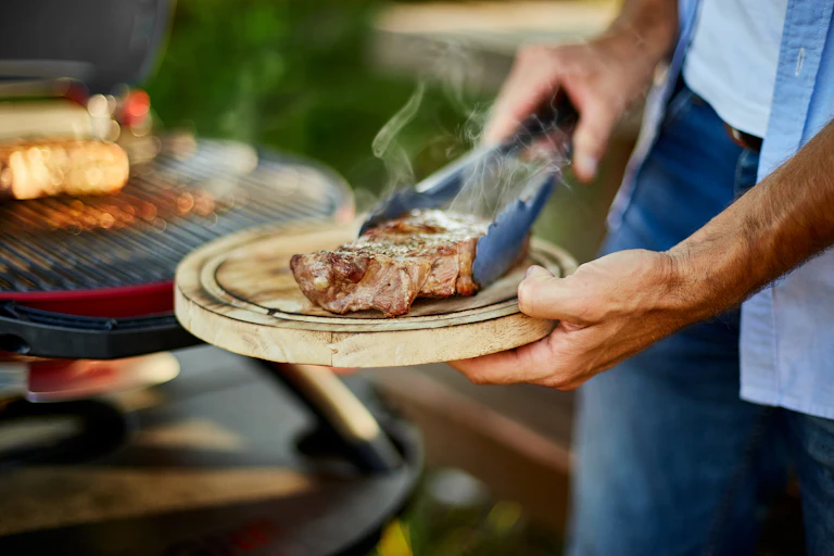Man holding a wooden board with a smoking steak on it.
