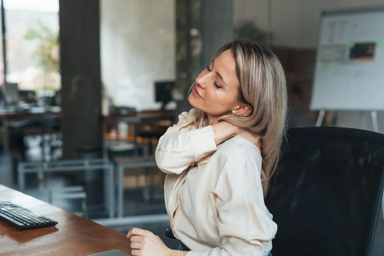 Femme d’âge mûr assise près de son ordinateur, se frottant le cou