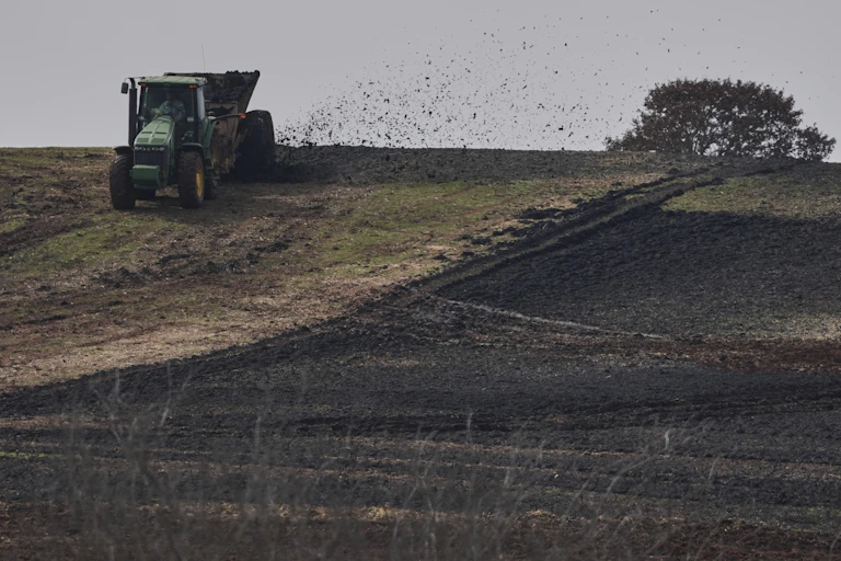 A tractor pulls a piece of equipment spraying material over a field.