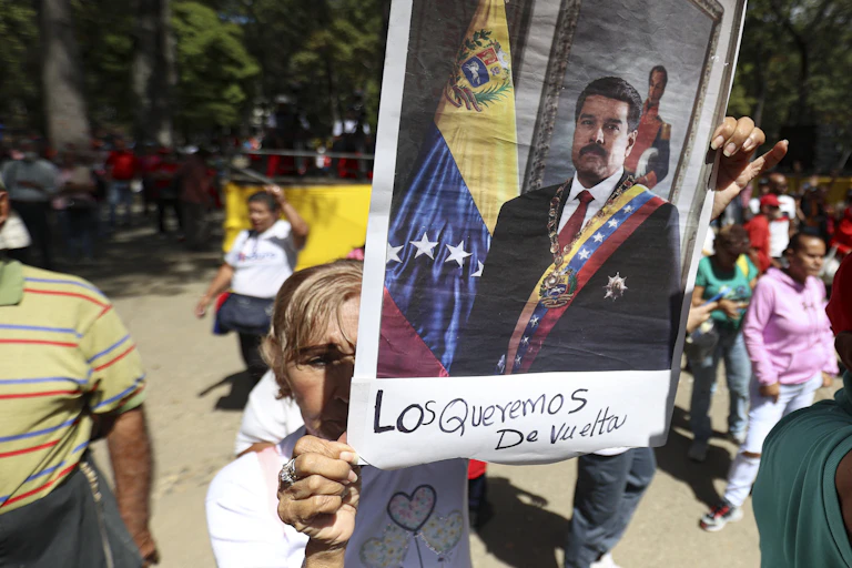 An older woman holds up a large photo of a man wearing a suit with a flag that is yellow, blue and red behind him.
