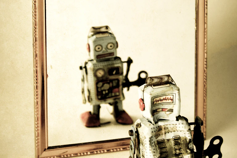 A wind-up toy robot looking in a mirror