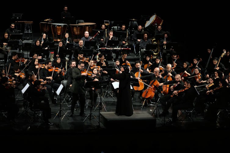a woman in a long black dress conducts an orchestra