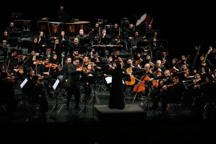 a woman in a long black dress conducts an orchestra