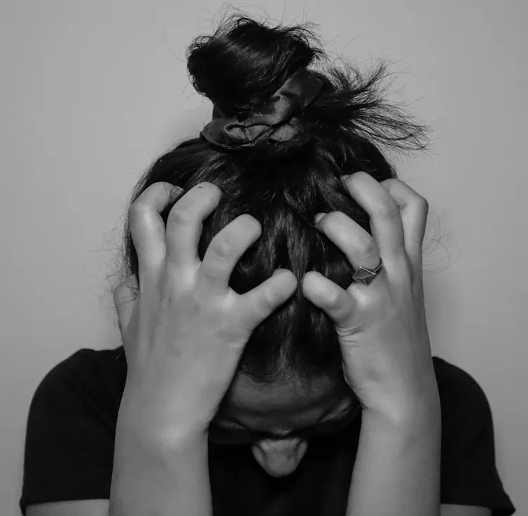 Young woman appears stressed, holding her head in her hands.