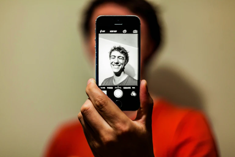 A man taking a smartphone selfie and the image on the phone is black and white.