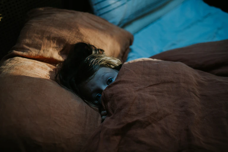 A child lies in bed and peers out of a doona.