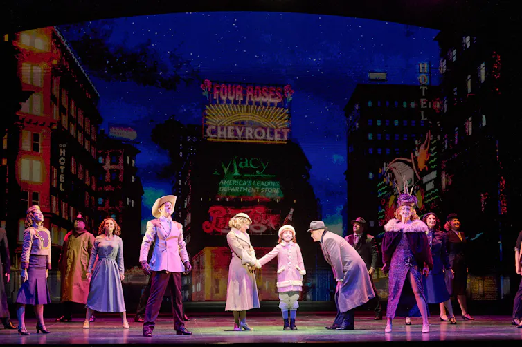 A child and adults on a theatre stage, lit but spotlights
