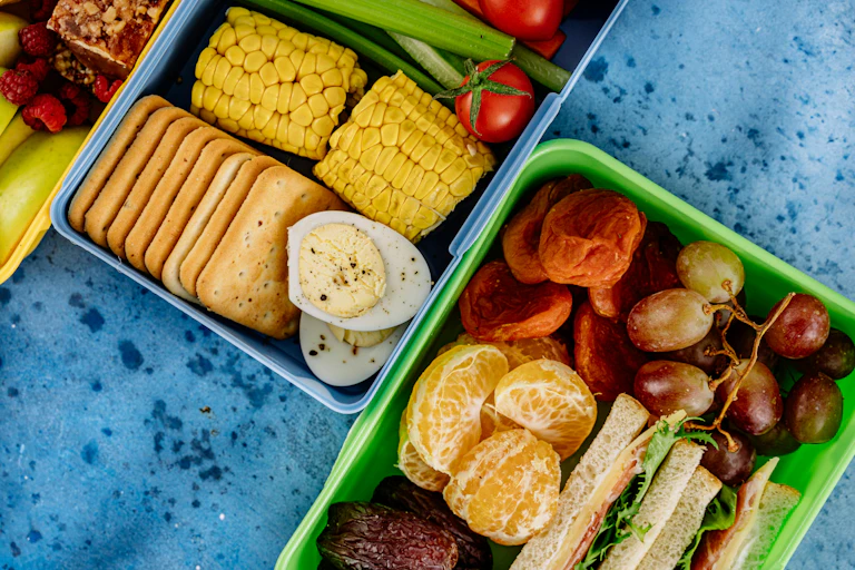 Lunchboxes with cut up fruit, vegetables, dried fruit a sandwich and crackers.