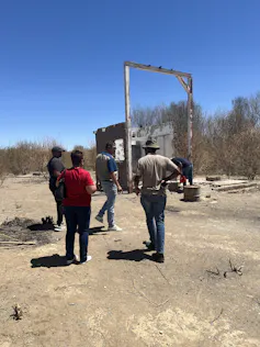People standing on dry, bare ground, with plants in the background