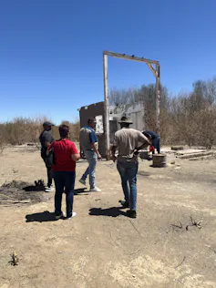 People standing on dry, bare ground, with plants in the background