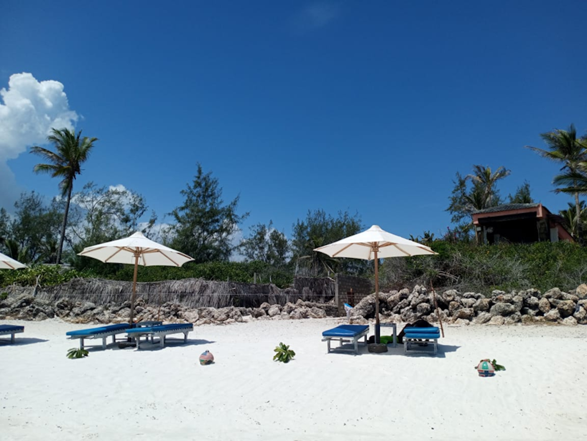 Loungers and umbrella on a beach, with a stone wall in the background
