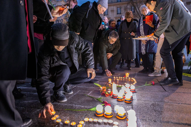 Candles being lit by a kneeling person at a vigil in support of Iranian protest.