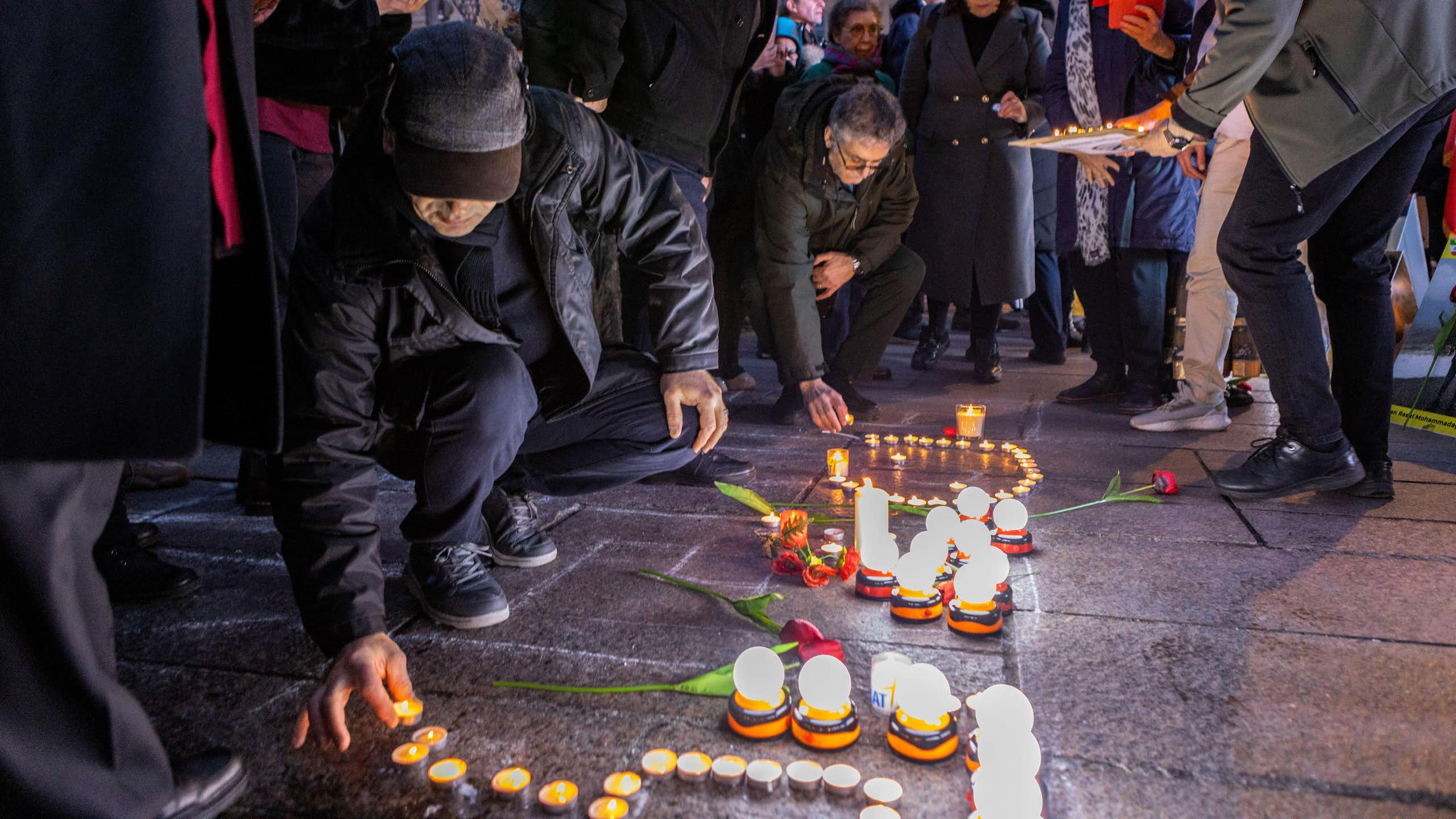 Candles being lit by a kneeling person at a vigil in support of Iranian protest.
