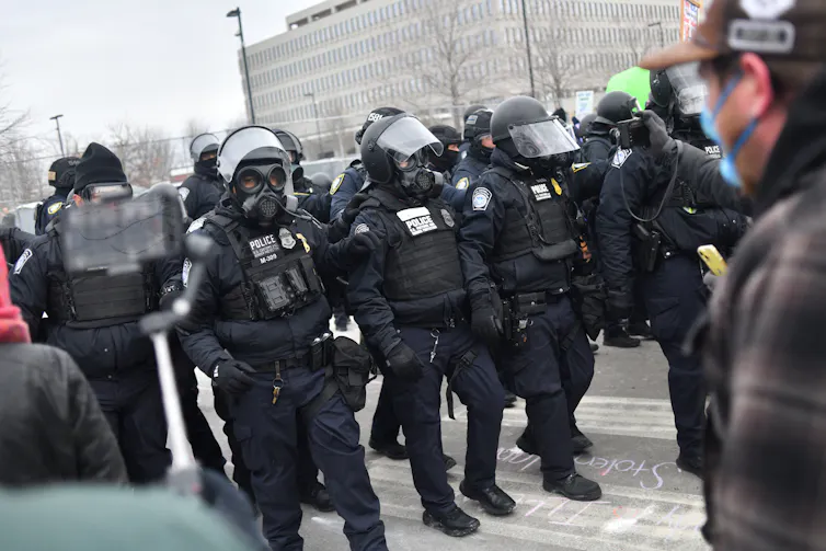 Agents dressed in military gear confront protestors.