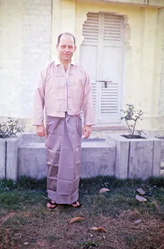 A man in a Burmese attire standing in a front of a white door.