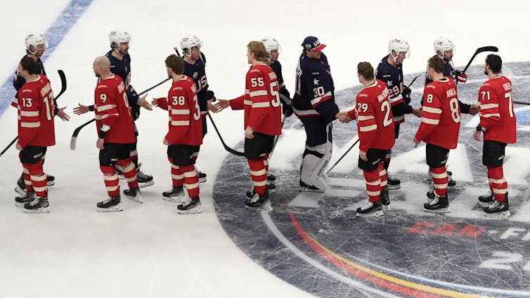 Un grupo de jugadores de hockey vestidos de rojo se dan la mano con jugadores de hockey vestidos de azul en la pista de hielo