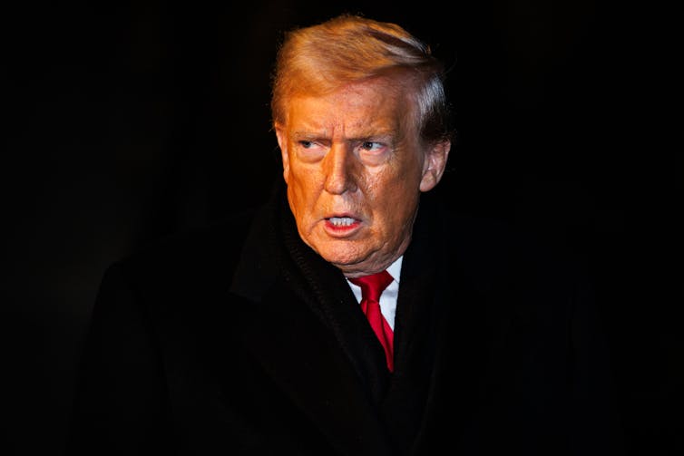 A man in a suit and red tie stands.
