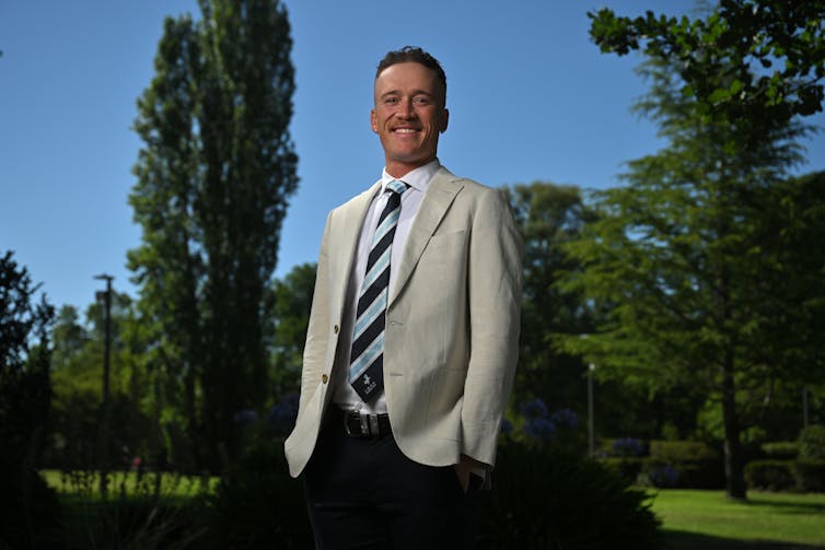 A young man in a blazer and tie smiles broadly