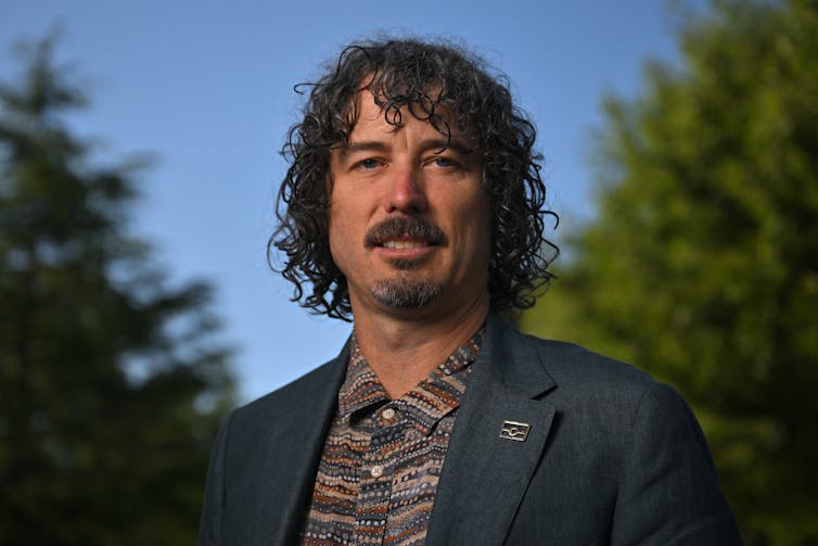 A curly-haired man smiles outside