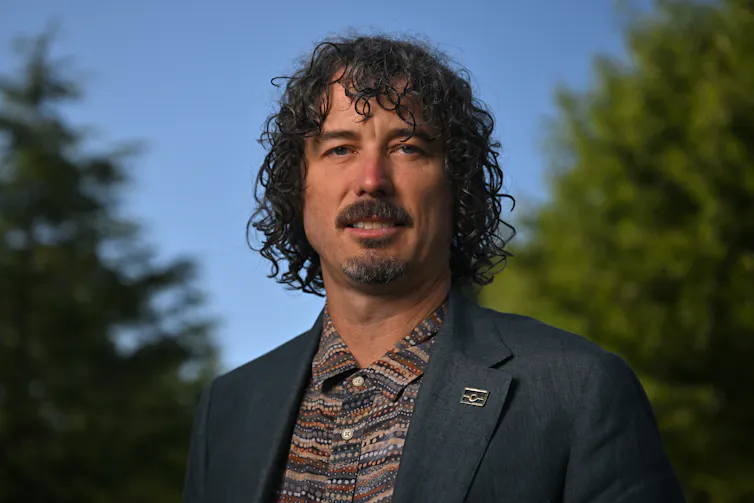 A curly-haired man smiles outside