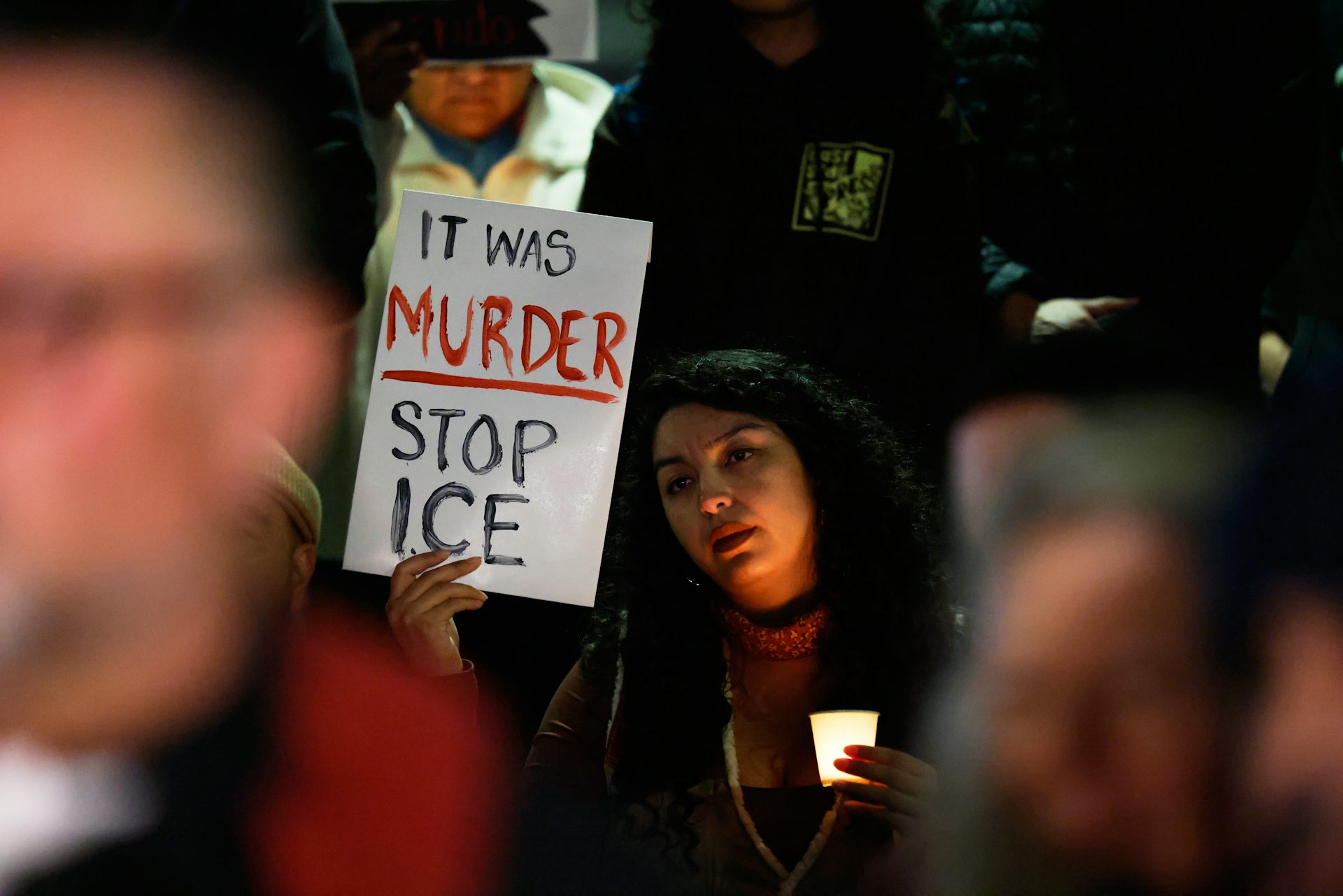 A woman holds a sign that reads 'it was murder, stop ICE.'