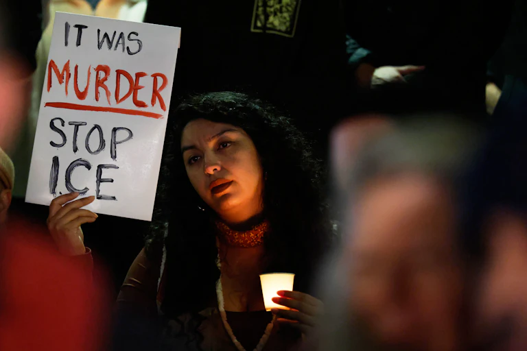 A woman holds a sign that reads 'it was murder, stop ICE.'