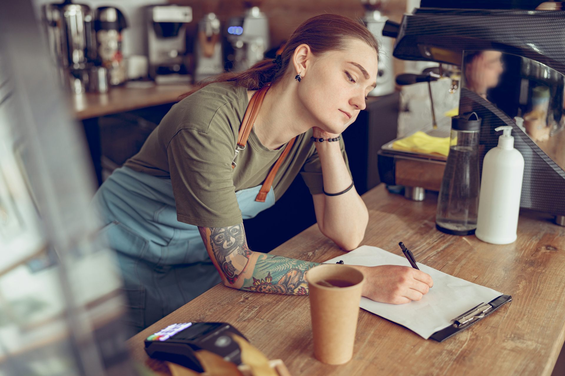 Young woman working in cafe writing on clipboard