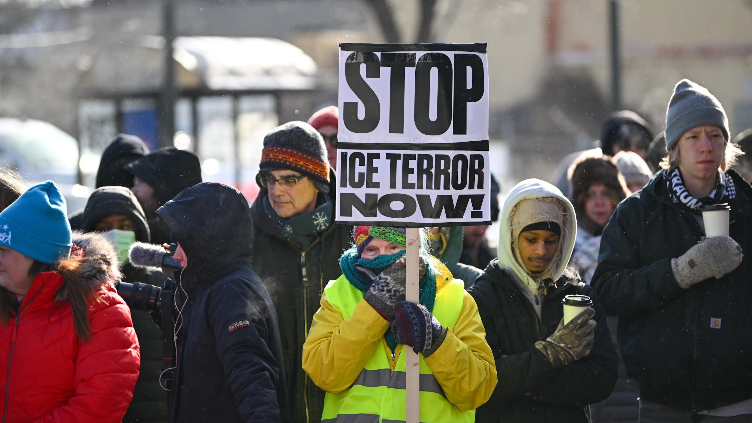 A woman holds a sign reading 'Stop ICE terror now!' at a memorial for Alex Pretti.