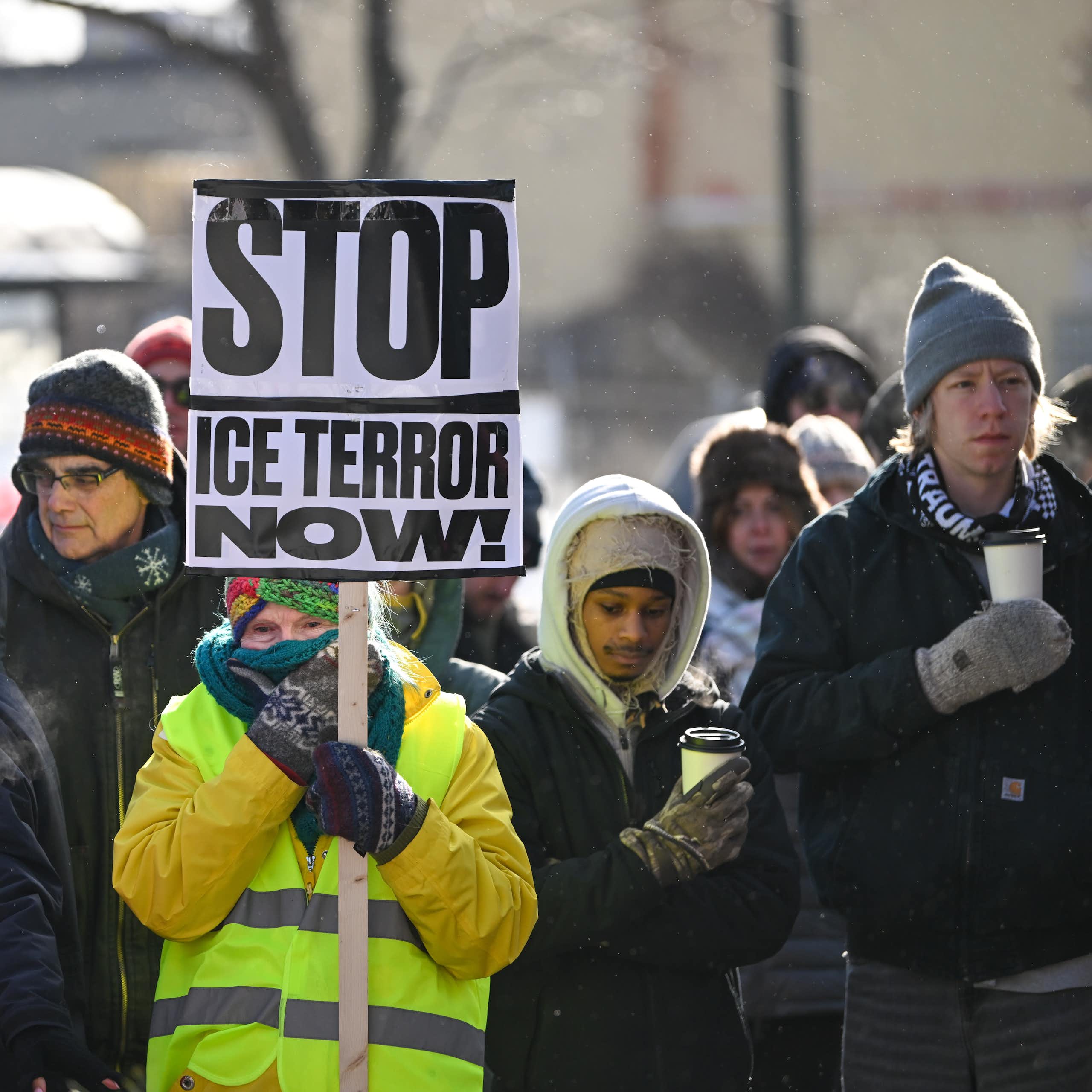 A woman holds a sign reading 'Stop ICE terror now!' at a memorial for Alex Pretti.
