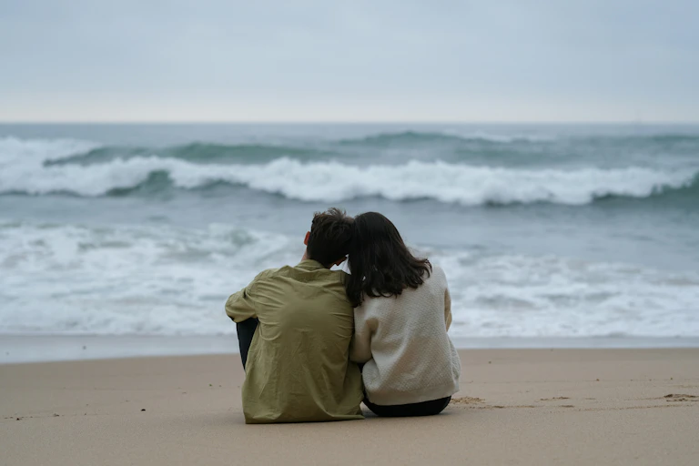 Un couple assis sur le sable, face à la mer