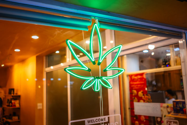 A neon sign in the shape of a marijuana leaf announces a cannabis store.
