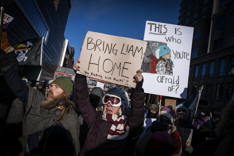 People dressed in winter clothing stand close together and hold signs that say 'Bring Liam home'