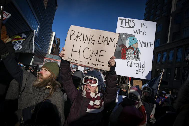 People dressed in winter clothing stand close together and hold signs that say 'Bring Liam home'