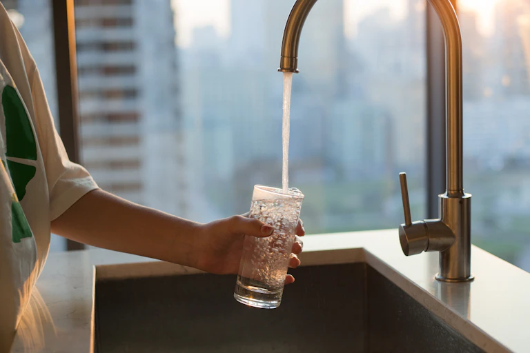 woman filling a glass with water from a kitchen tap.
