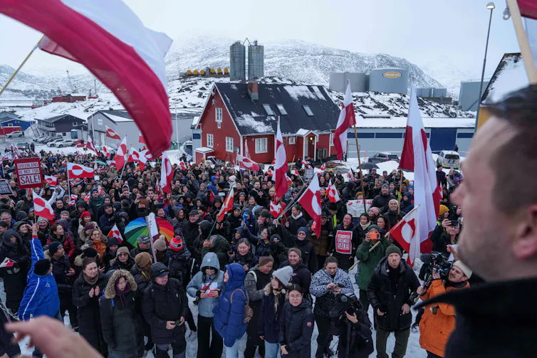 People gather outdoors carrying red and white flags.